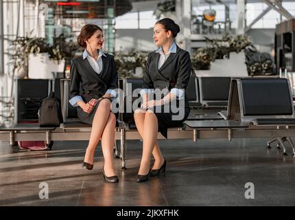 Zwei Flugbegleiter sitzen auf den Sitzen und unterhalten sich im Flughafenterminal Stockfoto