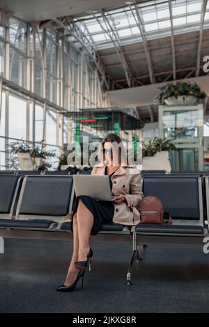 Junge Frau mit Laptop sitzt in der Wartehalle am Flughafen Stockfoto