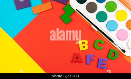 Eine Palette von Aquarellfarben, Alphabeten und Formen auf farbigem Hintergrund. Selektiver Fokus auf das Alphabet. Stockfoto