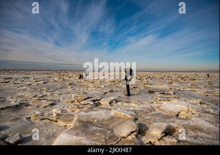 Ein Fotograf, der auf Eisschollen im gefrorenen Wattenmeer fotografiert Stockfoto