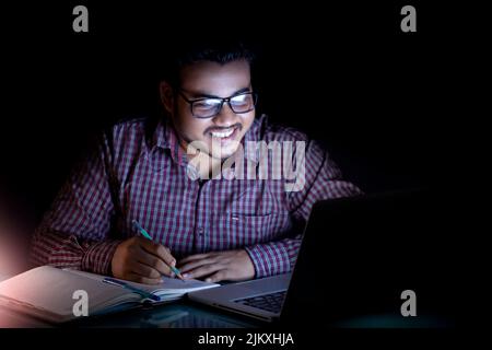 Junger Mann, der spät in der Nacht arbeitete und lächelte und auf den Bildschirm schaute Stockfoto
