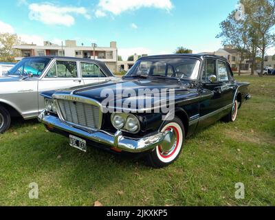 Chascomus, Argentina - Apr 09, 2022 - alte schwarze Plymouth Valiant von Chrysler Anfang 1960s kompakte viertürige Limousine. Grüne Natur Gras und Bäume backgro Stockfoto