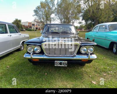 Chascomus, Argentina - Apr 09, 2022 - alte schwarze Plymouth Valiant von Chrysler Anfang 1960s kompakte viertürige Limousine. Vorderansicht. Grill. Grüne Natur Gras Stockfoto