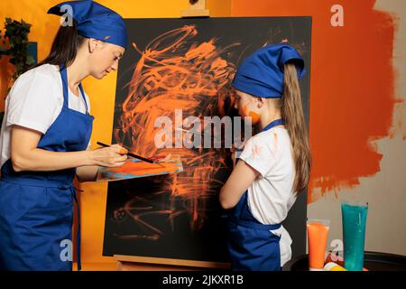 Erwachsene und Kinder mit oranger Farbe auf Leinwand, Malerei künstlerische Meisterwerk mit Aquarell, nasse Farbe aus Palette und Pinsel. Erstellen Sie farbenfrohe Kunstwerke mit Fähigkeiten und kreativer Vision. Stockfoto