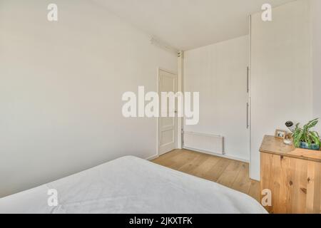 Komfortables Bett mit gepunkteter Federdecke in der Nähe von Kleiderschrank und Tisch mit Stuhl im minimalistischen Stil im modernen Apartment Stockfoto