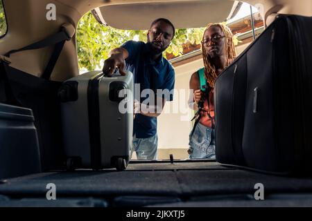 Freund und Freundin, die Reisetaschen und Trolley in den Kofferraum, immer bereit, in den Urlaub mit dem Auto zu verlassen. Reisen mit dem Auto auf Autotour mit Gepäck und Koffern. Stockfoto