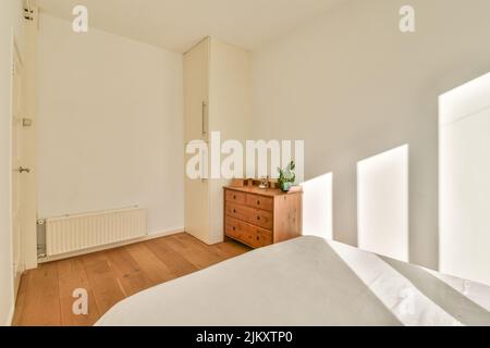 Komfortables Bett mit gepunkteter Federdecke in der Nähe von Kleiderschrank und Tisch mit Stuhl im minimalistischen Stil im modernen Apartment Stockfoto