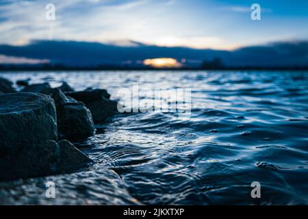 Eine malerische Aussicht auf die Felsen am Seeufer mit Bäumen am Horizont gegen Abendhimmel bei Sonnenuntergang in Frederick, Colorado, USA Stockfoto