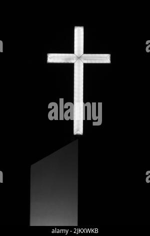 Eine vertikale Aufnahme eines in einem dunklen Hintergrund beleuchteten Kirchenkreuzes
