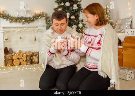 Weihnachten, ein Mann und eine Frau in identischen Pullovern, trinken Tee unter einer Decke Stockfoto