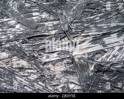 Spanplatte in schwarzer Farbe. Hintergrund von einem bemalten Brett. Muster. Holzhintergrund. Komprimierte Chips. Alte, schäbige Wand, blätternde Farbe Stockfoto