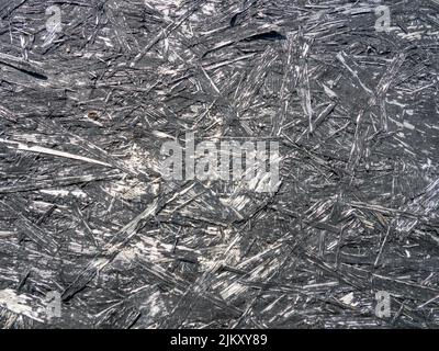 Spanplatte in schwarzer Farbe. Hintergrund von einem bemalten Brett. Muster. Holzhintergrund. Komprimierte Chips. Alte, schäbige Wand, blätternde Farbe Stockfoto