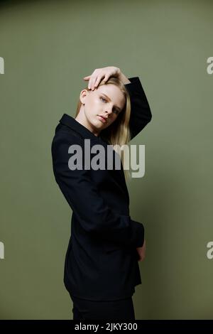 Cooles Banner für Marken. Ein attraktives, cooles Profi-Model posiert in einer Halbdrehung und blickt auf einem grünen olivgrünen Hintergrund im Studio auf die Kamera Stockfoto