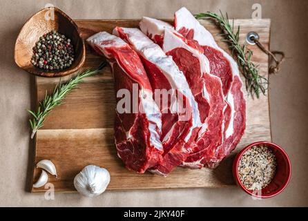 Eine Draufsicht auf Scheiben rohes Fleisch auf einem Holzbrett mit Gewürzen Stockfoto