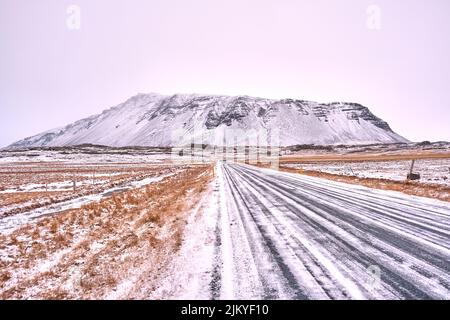 Winterszene der langen geraden Straße zum schneebedeckten Berg in Island Stockfoto