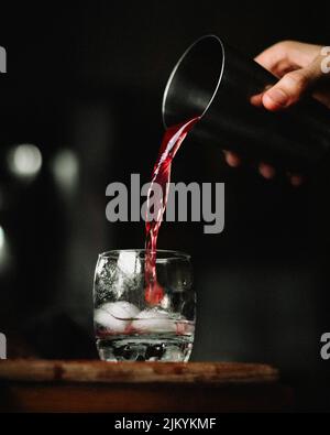 Eine vertikale Aufnahme von rotem, kirschrotem, alkoholischem Getränk mit Eis unter Beleuchtung auf schwarzem Hintergrund Stockfoto