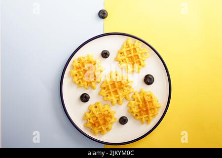 Waffelstücke mit Brombeeren auf einem Teller auf einer weißen und gelben Oberfläche Stockfoto