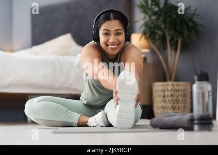 Ich beginne jeden Morgen mit einem schnellen Training. Porträt einer sportlichen jungen Frau, die ihre Beine während des Trainings zu Hause streckt. Stockfoto