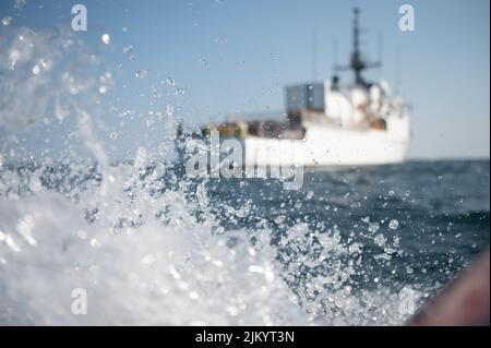 Eine Detailaufnahme zeigt das Wasser, das im Vordergrund spritzt, mit dem USCGC Bear (WMEC 901), der im Hintergrund die Gewässer des Atlantischen Ozeans patrouilliert, 22. Juli 2022. Der Bear und seine Crew arbeiten zusammen, um die Organisation für die Fischerei im Nordatlantik zu unterstützen, illegale Fischerei abzuschrecken und gemeinsam mit seinen Partnerländern das Bewusstsein für den maritimen Bereich zu schärfen. (USA Foto der Küstenwache von Petty Officer, Klasse 3., Matthew Abban) Stockfoto