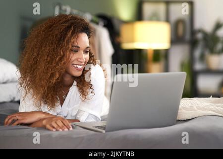 Ich hoffe, diese E-Mail findet Sie gut, es tut. Eine junge Frau, die ihren Laptop benutzt, während sie auf ihrem Bett liegt. Stockfoto