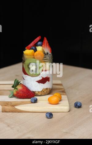 Ein köstlicher Chia-Parfait mit verschiedenen Früchten in einem Glas auf einem Holzbrett auf einem Tisch Stockfoto