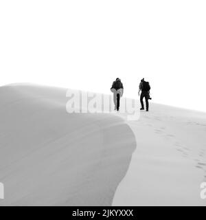 Eine Graustufenaufnahme von zwei Menschen, die in einer Wüste wandern Stockfoto