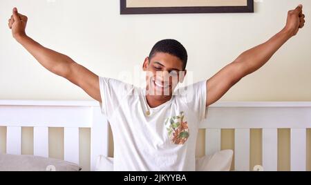 Erhebt euch und glänzt schlafend. Ein hübscher junger Mann sitzt im Bett und dehnt sich in den frühen Morgenstunden. Stockfoto