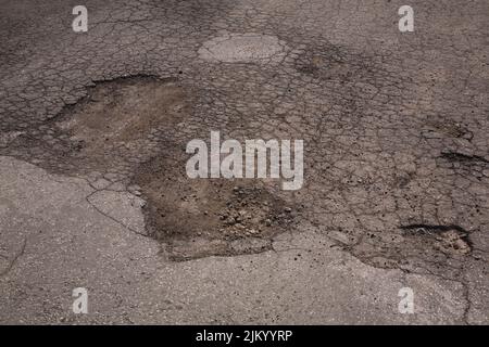 Nahaufnahme von gebrochenem Asphaltbelag mit Schlaglöchern. Stockfoto