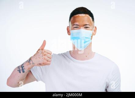 Indem ich mich um mich selbst kümmere, kümmere ich mich um Du auch. Portraitaufnahme eines jungen Mannes mit Vitiligo, der eine schützende Gesichtsmask trägt und auf weißem Hintergrund posiert. Stockfoto