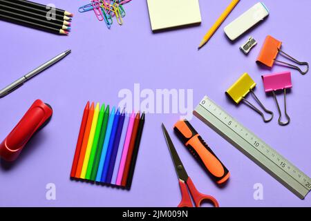 Eine Draufsicht auf eine Reihe von Schulmaterialien wie Binderclips, Buntstifte und Bleistifte auf mauvem Hintergrund Stockfoto