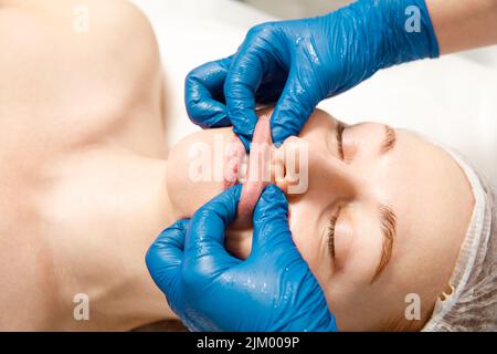 Eine verjüngende Behandlung für die Gesichtshaut. Der Kosmetologe macht eine bukkale Massage der Gesichtsmuskeln des Patienten. Stockfoto