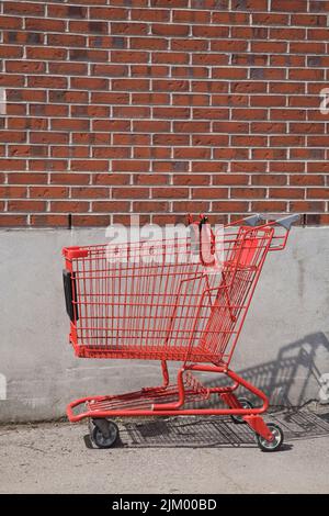 Verlassener roter Einkaufswagen an einer Backsteinmauer in einer Hintergasse. Stockfoto