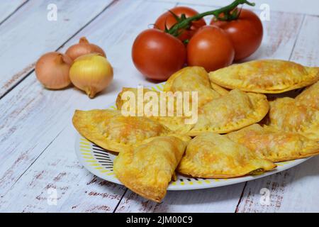 Eine Nahaufnahme von Thunfisch-Empanadas auf einem Teller mit Tomaten und Zwiebeln auf rustikalem weißen Hintergrund Stockfoto