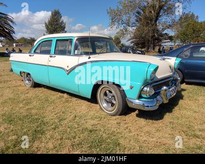 Chascomus, Argentinien - 9. Apr 2022: Zweifarbiger Ford Fairlane Town Sedan V8, blau und weiß, viertürig 1955. Natur grünes Gras und Bäume Hintergrund. C Stockfoto