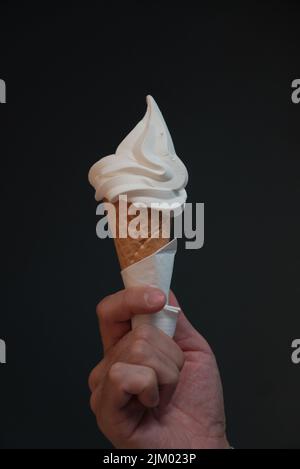 Eine vertikale Nahaufnahme einer Hand, die einen Eiskegel vor einem schwarzen Hintergrund hält Stockfoto