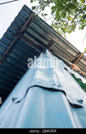 Ein Bottom-up-Foto einer Ecke eines Dorfhauses aus GCI-Blättern. Das Dach des Hauses besteht ebenfalls aus GCI-Platten. Stockfoto