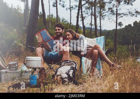 Junge Männer und Frauen, die auf einem Stadtplan sitzen, während sie auf ihrem Campingplatz sitzen. Abenteuerliches junges Paar, das im Freien in der Natur campen kann. Stockfoto