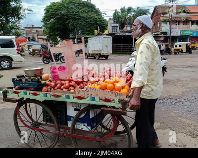 Kolhapur, Indien- Juli 16. 2021; Stock Foto von 50 bis 60 Jahre alten indischen Obstverkäufer verkauft frische Früchte wie Apfel , Orange usw. auf Holzwagen in c Stockfoto