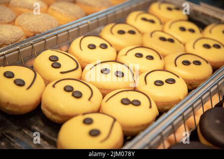 Eine Nahaufnahme von süßen Donuts mit gelb lächelnden Gesichtern auf dem Regal in einer Konditorei Stockfoto