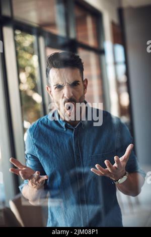 Wütender, gestresster und frustrierter Mann, der unglücklich ist und sich über Arbeitsprobleme schlecht fühlt, während er allein in einem modernen Büro steht. Aggressiv, verärgert und verärgert Stockfoto
