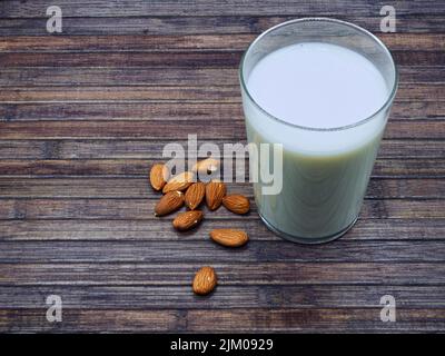 Nahaufnahme eines Glases Mandelmilch auf einem Holztisch und ein paar Mandeln im Vordergrund Stockfoto