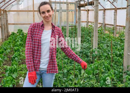 Hübsche Kindergärtnerin mit roter Arbeit Handschuhportrait im Gewächshaus Stockfoto