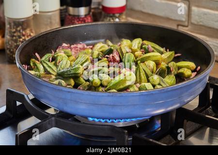 Okra und gebratene lila Zwiebeln werden in einer Pfanne auf einem Gasherd gebraten. Stockfoto