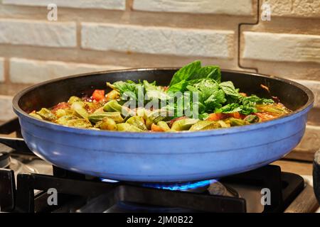 Okra und gebratene lila Zwiebeln werden mit Koriander und Basilikum auf dem Gasherd in der Pfanne gebraten. Stockfoto