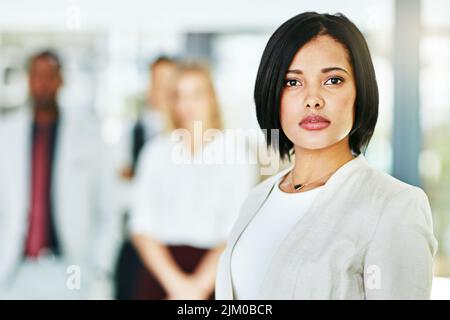 Seriöse, fokussierte und selbstbewusste Rechtsanwältin, die die Kamera anschaut und mit ihrem Team in ihrem Büro steht. Porträt eines Führers, smart und Stockfoto