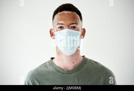 Masken sind eine einfache Barriere, um die Ausbreitung einzudämmen. Studioporträt eines jungen Mannes mit Vitiligo, der eine Maske auf weißem Hintergrund trägt. Stockfoto