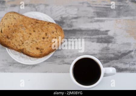 Ein Blick von oben auf eine Tasse Kaffee mit Brotscheiben auf einem grauen Tisch Stockfoto