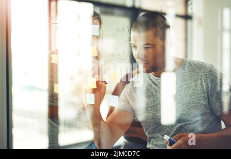Ich habe eine klare Vision von dem, was ich will. Aufnahme eines Mannes, der mit seinem Team hinter ihm Ideen auf Haftnotizen schreibt. Stockfoto