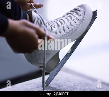 Schlittschuhe über Stilletos. Eine nicht erkennbare Figur Skater Band die Schnürsenkel auf ihre Schlittschuhe. Stockfoto