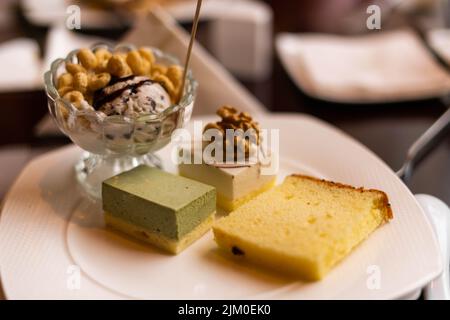 Eine flache Aufnahme verschiedener Dessertsorten auf einem Teller mit Eis, Kuchen und Nüssen im Café Stockfoto
